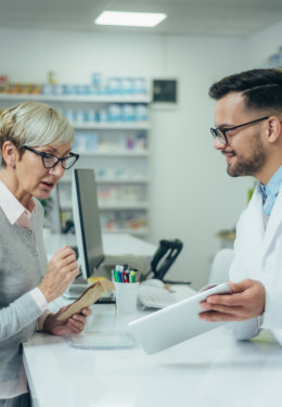 Happy senior woman customer buying medications at drugstore while talking with a male pharmacist